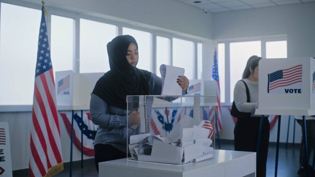 An American Muslim woman in hijab puts ballot paper in box.